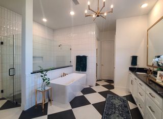 A luxurious bathroom featuring a tiled bathtub, glass shower, and checkered flooring with modern gold fixtures.