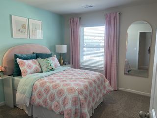 A charming bedroom with a pastel palette, featuring a plush pink headboard, patterned bedding, and a full-length arched mirror reflecting natural light.