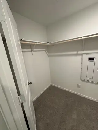 A spacious walk-in closet with carpeted flooring and white walls, featuring ample hanging rods for organized storage.