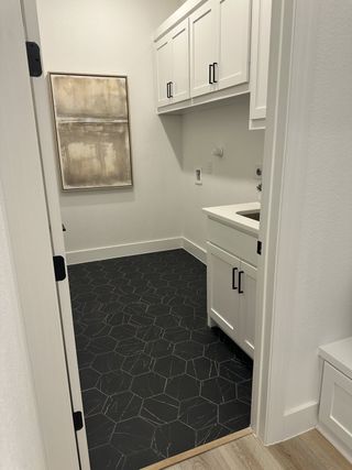 Model Home A sleek laundry room with hexagonal black tile flooring, white cabinets, and modern artwork.