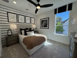 A modern bedroom with a striped accent wall, cozy bed, stylish artwork, and ample natural light.