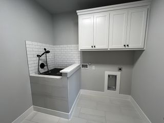 Model Home A sleek laundry room with a pet wash area, white cabinetry, subway tile, and modern fixtures.