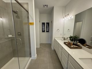 A spacious bathroom featuring a glass-enclosed shower, dual sinks with white cabinetry, and elegant lighting fixtures.