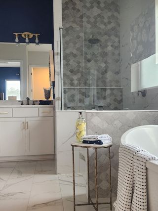 Model Home A chic bathroom featuring a marble-tiled shower, deep bathtub, elegant vanity, and modern lighting.