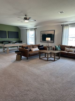A spacious living room with brown sofas, a pool table, and modern decor, featuring neutral tones and abundant natural light.