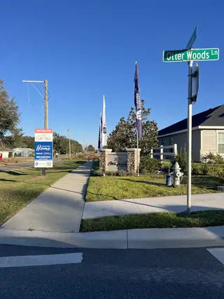 A welcoming entrance to Otter Woods Estates by Highland Homes of Florida in Auburndale, FL, featuring lush landscaping and clear skies.