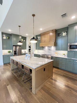 A modern kitchen featuring green cabinetry, a spacious marble island, and elegant pendant lighting.