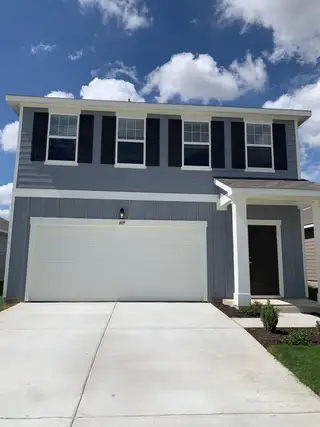 Street view A modern gray two-story home with black shutters and a spacious driveway in Hymeadow by Starlight Homes (Maxwell, TX).