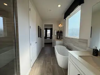 A modern bathroom with a freestanding tub, sleek white cabinetry, and large windows for natural light.