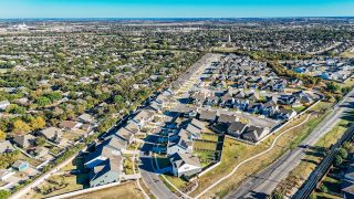 Aerial view of Brooks Ranch community showcasing modern homes by D.R. Horton in Kyle, TX amid lush greenery and winding roads.
