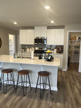 A modern kitchen with white cabinets, stainless steel appliances, a sleek island with seating, and a spacious pantry.