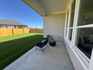 A cozy covered patio with two black chairs, a small table, and a view of a fenced, freshly landscaped yard.
