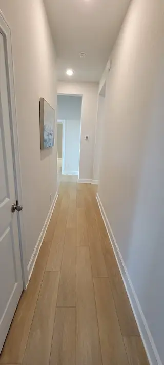 A bright hallway with light wood flooring, white walls, and modern recessed lighting.