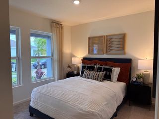 A cozy bedroom with a plush navy bed, warm lighting, and modern decor, featuring large windows with a view.