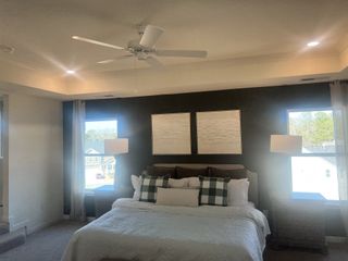 A cozy bedroom with a dark accent wall, large windows, and stylish decor, featuring a plush bed and modern lighting.