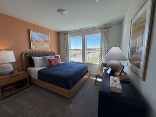 A cozy bedroom with a woven bedframe, colorful pillows, warm lighting, and large windows for natural light.