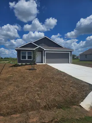 Street view A modern gray home with a spacious driveway and youthful landscaping in Schriber Ranch by Lennar (Mustang Ridge, TX).