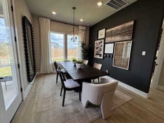Model Home A modern dining room with a sleek table, stylish chairs, black accent wall, and large windows overlooking a backyard.