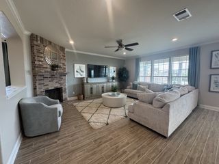 A living room featuring an Ashley sectional in a neutral tone, a brick fireplace, a round coffee table, and wood-look tile flooring.