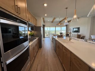 Model Home A modern kitchen with stainless steel appliances, a large island with a sink, pendant lighting, and an open layout leading to the living area.