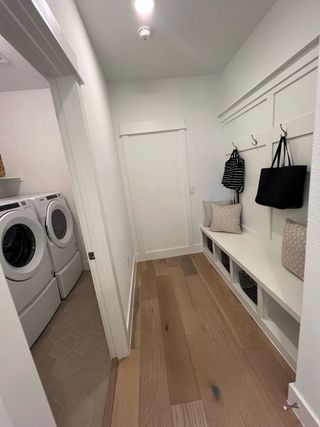 A functional mudroom with storage bench, hooks, and a view of a modern laundry area with washer and dryer.