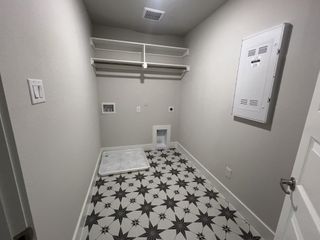 A functional laundry room featuring stylish patterned floor tiles, open shelving, and ample utility connections.
