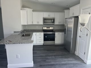 A modern kitchen featuring sleek white cabinets, speckled granite countertops, and stainless steel appliances.