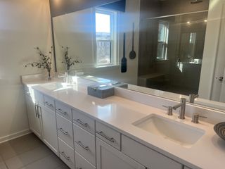 A bright bathroom features a dual vanity with white cabinetry and a quartz countertop, complemented by a large mirror and a glass-enclosed shower.