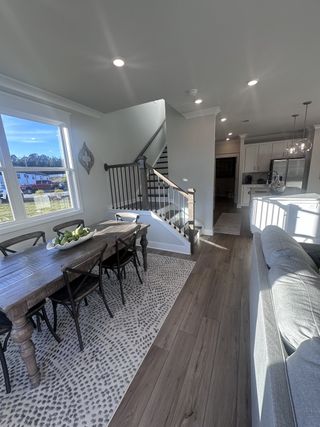 Model Home A cozy dining area with a rustic wooden table, modern railing staircase, and bright natural light on wood floors.
