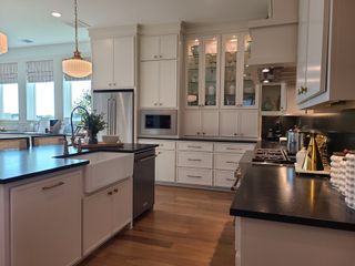 A modern kitchen featuring sleek black countertops, elegant white cabinetry, and warm hardwood flooring.