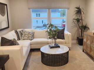 A cozy living room with a white sectional, chic throw pillows, a round coffee table, and lush greenery by the window.