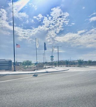 Community Amenities A sunny street view with flags flutters in Monroe Ranch by K. Hovnanian® Homes in Buckeye, AZ, under a vibrant sky.