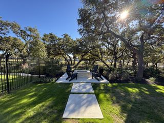 A scenic backyard with a paved fire pit area, Adirondack chairs, and lush greenery.