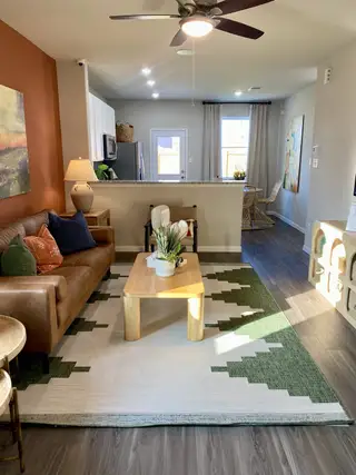 Model Home A cozy living area with a leather sofa, patterned rug, wooden coffee table, and modern kitchen in the background.