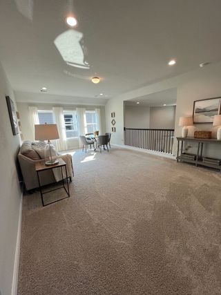 Model Home A cozy carpeted loft with natural light, a comfortable sofa, and seating by the window creates a warm, inviting space.