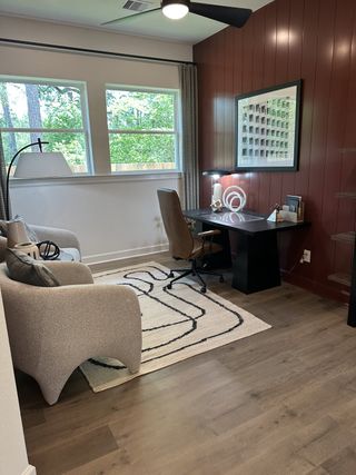 A cozy home office with a textured accent wall, sleek desk, modern chair, and large windows overlooking greenery.