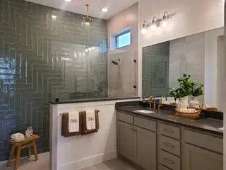 A chic bathroom featuring herringbone tiles, brass fixtures, and a dual-sink vanity with elegant lighting.