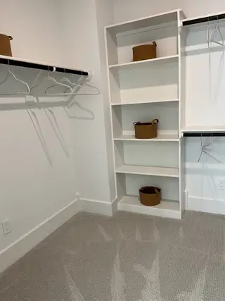 Model Home A spacious walk-in closet with carpeted flooring, open shelving, and hanging rods for ample storage.