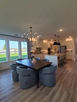 A modern dining area with plush chairs, a sleek dark table, and an open kitchen illuminated by elegant lighting.
