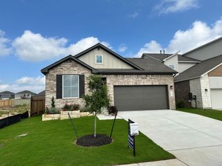 Street view A charming brick home with sleek garage and lush lawn in Santa Rita Ranch by Scott Felder Homes (Liberty Hill, TX).