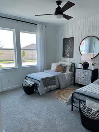 A cozy bedroom featuring twin beds, a patterned rug, modern fan, and soft gray accents.
