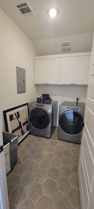 A modern laundry room featuring sleek appliances, white cabinetry, and geometric tiled flooring.