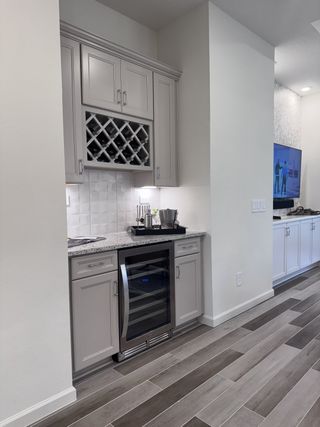 A sleek home bar with a wine rack, granite countertop, and wine cooler, complemented by elegant cabinetry and wood flooring.