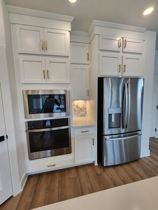 A modern kitchen with white cabinets, stainless steel appliances, and elegant brass handles, featuring a built-in oven and fridge.