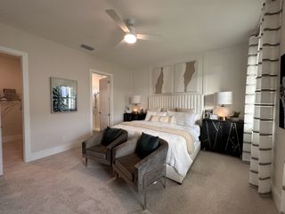 A chic bedroom featuring a plush bed, elegant artwork, and stylish lamps, complemented by soft carpeting and cozy seating.
