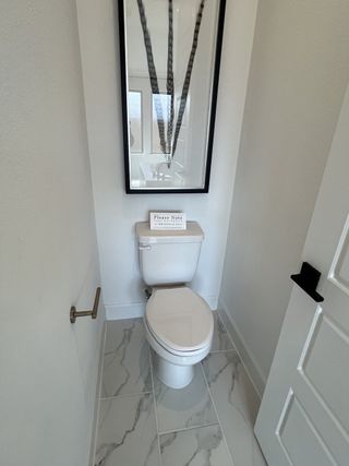 Model Home A modern bathroom with marble tile flooring, a sleek toilet, and elegant wall art.
