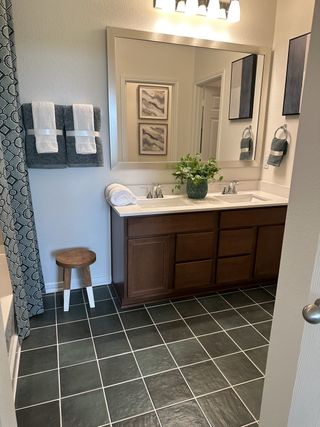 A modern bathroom featuring a large mirror, elegant dual sinks, dark tile flooring, and stylish decor.
