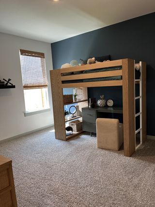 A cozy kids' room with a loft bed, dark accent wall, and functional desk space, accented by natural light and soft carpet.