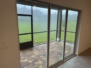 Model Home A cozy screened patio with brick flooring and large sliding glass doors, offering views of lush greenery.