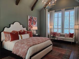 Model Home A cozy bedroom with vaulted ceilings, elegant chandelier, and rich floral decor, featuring a plush bed and seating area.
